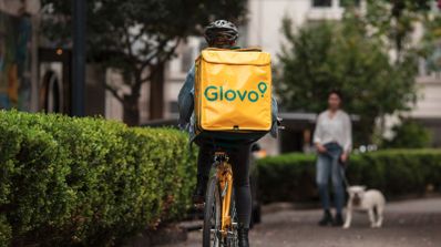Un rider de Glovo montando en bicicleta con la mochila de la marca