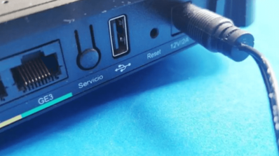 Persona utilizando la punta de un bolígrafo para presionar el botón de reset hundido en el panel trasero de un router de fibra