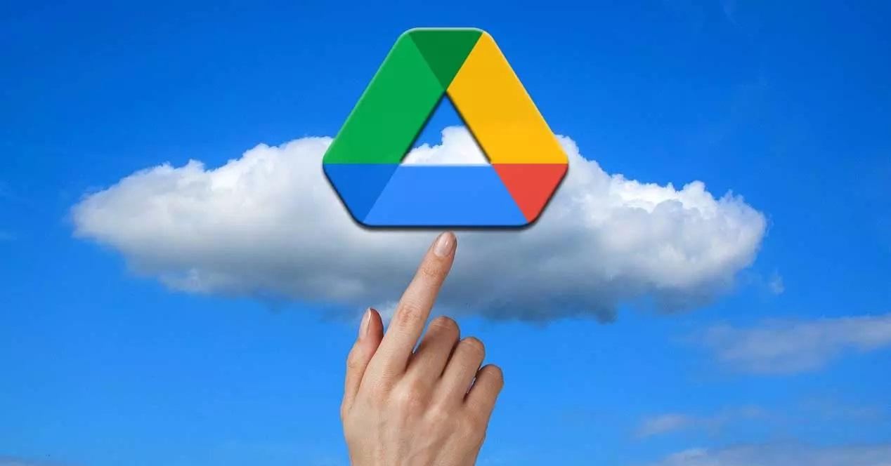 Una mano toca el icono de Google Drive sobre un fondo azul cielo con nubes.