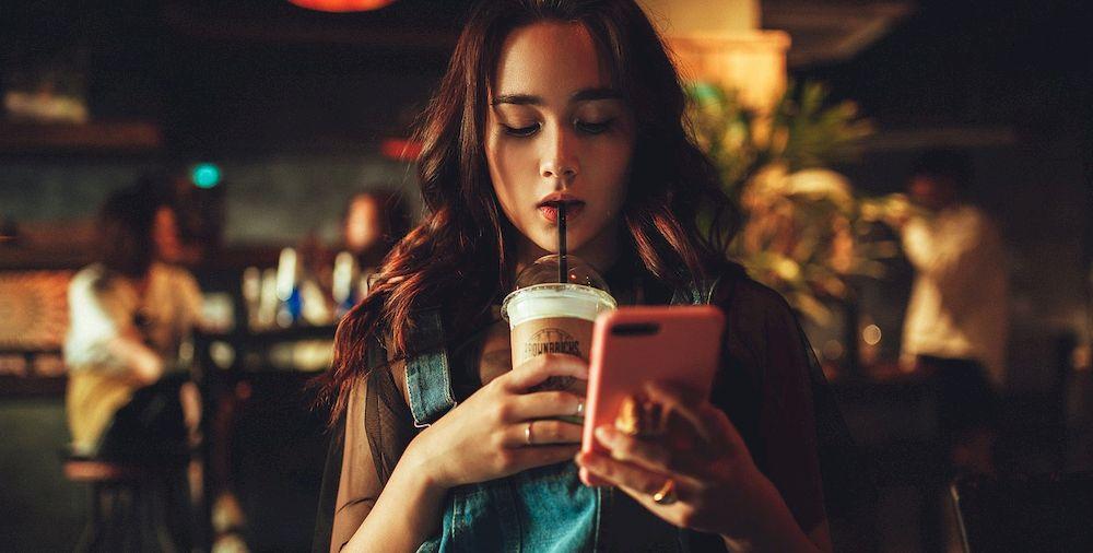 Una mujer bebe café y mira el móvil mientras tanto