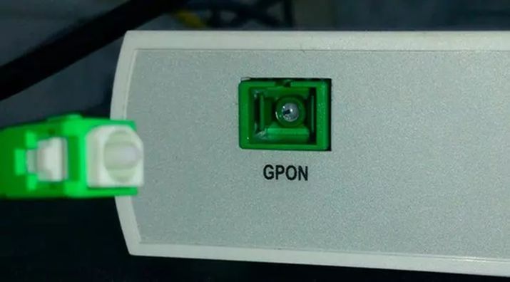 Primer plano de un puerto de entrada GPON en un dispositivo de red y un conector de fibra óptica verde.