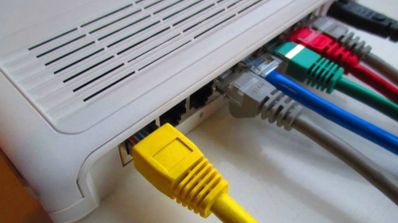 Varios cables Ethernet de colores amarillo, azul, gris y verde conectados a los puertos traseros de un router doméstico blanco.