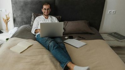 Un chico tumbado en la cama mientras utiliza el ordenador portátil