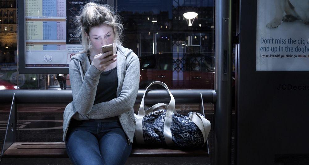 Mujer espera el autobús mientras utiliza su móvil