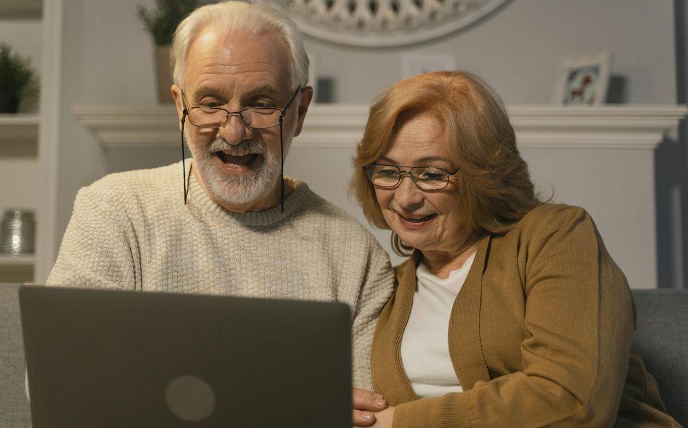 Una pareja de ancianos riéndose mientras miran el ordenador