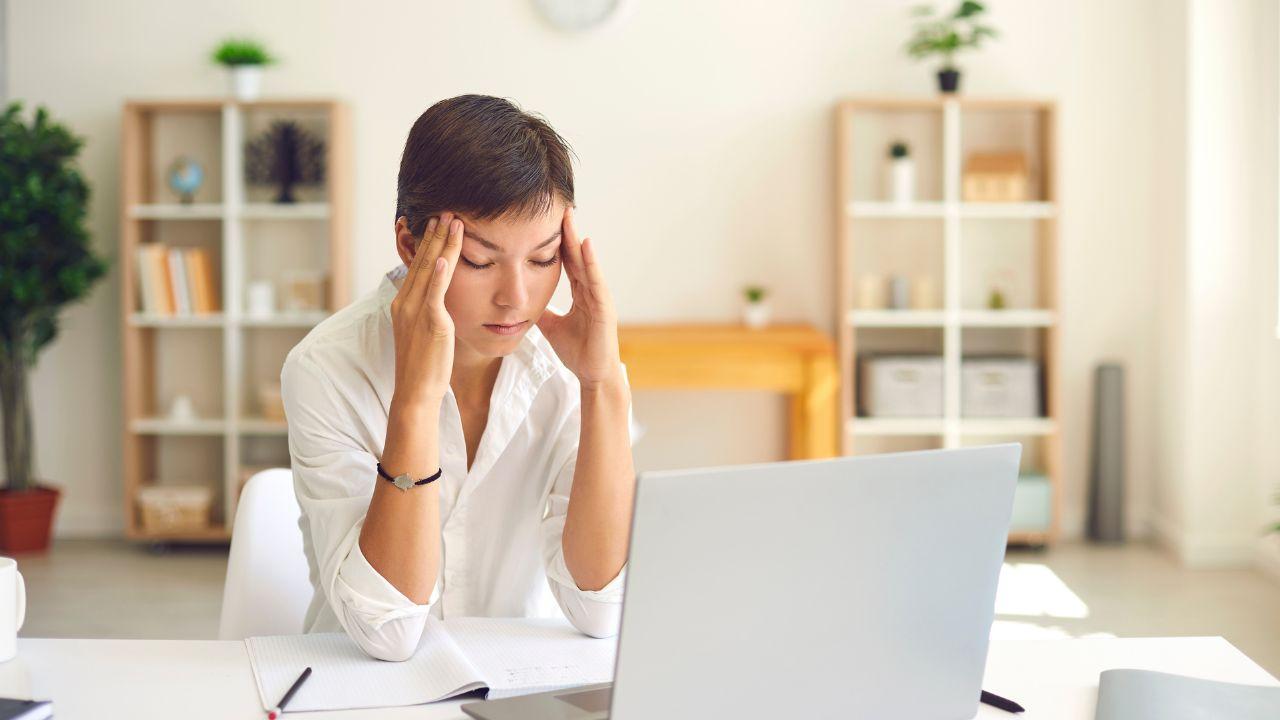 Una mujer sufre dolor de cabeza al leer una mala noticia en el portátil