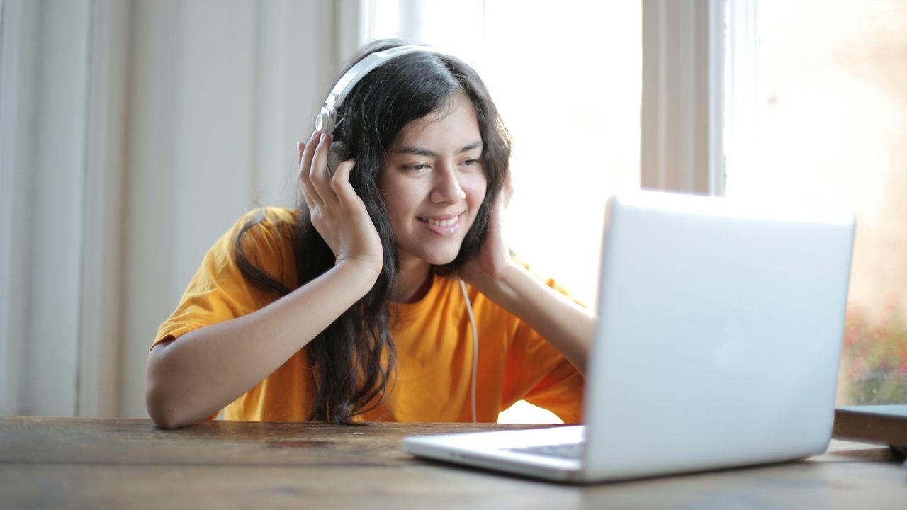 Chica utiliza su ordenador mientras está escuchando feliz un audiolibro