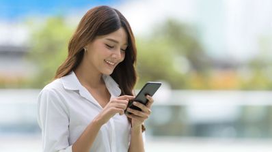 Chica feliz sonríe mientras está usando el teléfono móvil