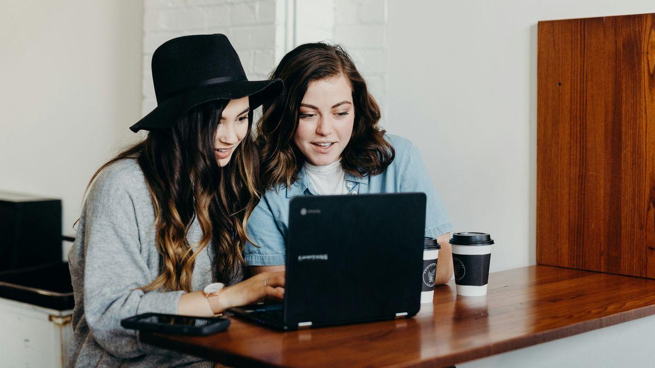 Dos amigas utilizan un ordenador portátil mientras toman café