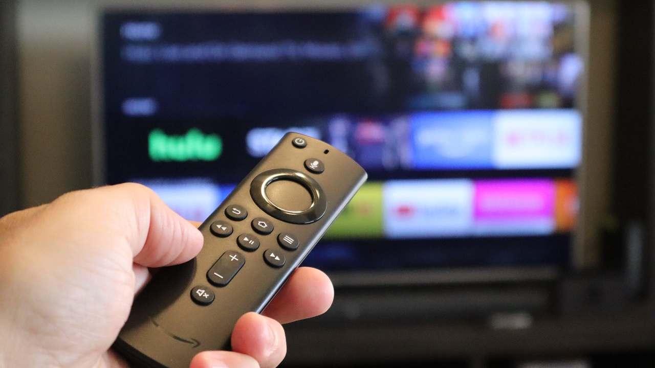 Una mano sujeta un Fire Stick apuntando a una televisión con Amazon Fire TV.