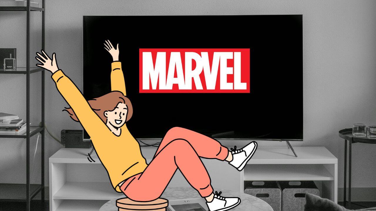 Una chica está alegre y se ve el logo de Marvel en una TV