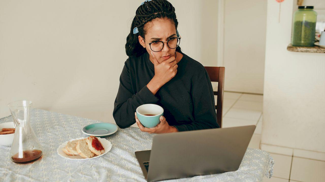 Una mujer está pensativa desayunando y mirando su ordenador
