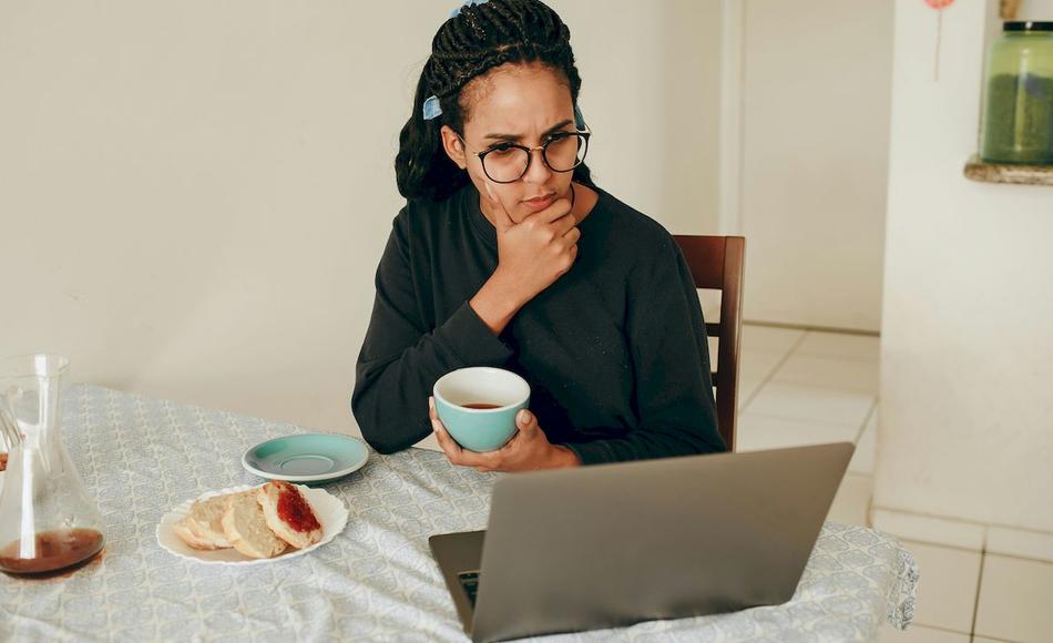 Una mujer está pensativa desayunando y mirando su ordenador