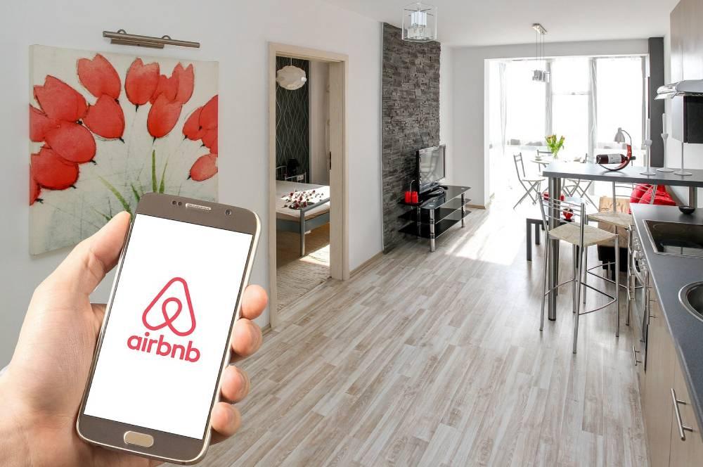 Mano sujetando móvil con logo de Airbnb en un apartamento turístico.