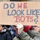 Un hombre lleva una pancarta que dice: "Do we look like bots?".