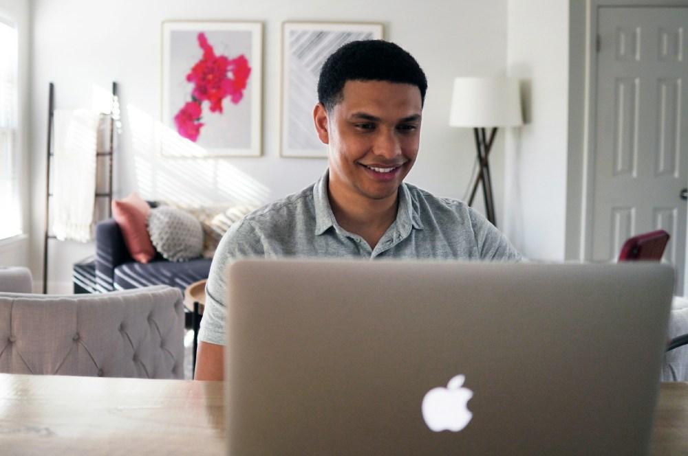 Hombre sonríe trabajando con un portátil Apple.