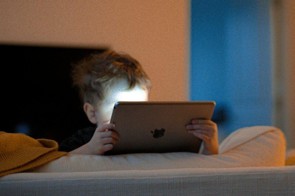 Un niño pequeño utiliza un iPad tumbado en la cama.