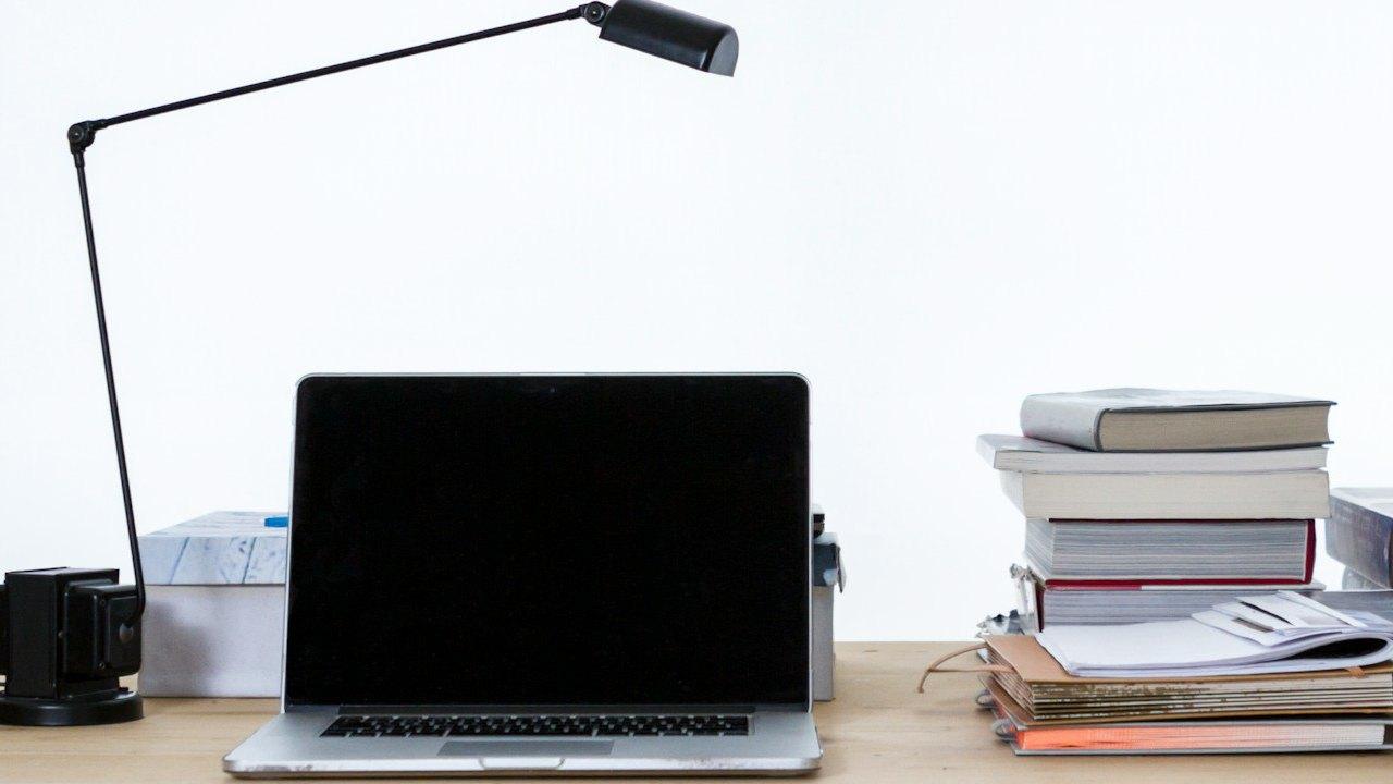 Un portátil abierto sobre un escritorio con libros y documentos al lado.