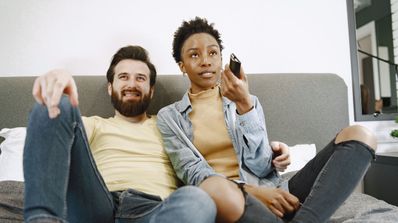 Una pareja está en el sofá viendo la televisión y cambiando de canal