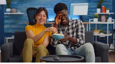 Una pareja riéndose en el sofá mientras comen palomitas