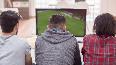 Grupo de aficionados al fútbol celebrando un gol mientras ven un partido de LaLiga 2025/2026 en televisión en el salón de una casa
