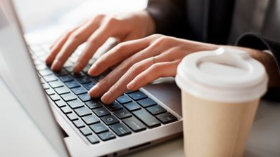 persona tecleando en un portatil de apple con un cafe