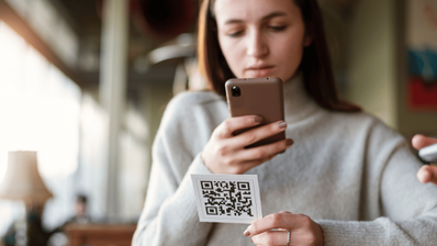 Persona usando su smartphone para escanear un código QR en un punto de recarga público para coches eléctricos, ilustrando el riesgo de estafas de QRishing.