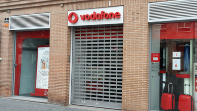 Fachada de una tienda de Vodafone en una calle de España, con el logotipo rojo corporativo y escaparates iluminados'