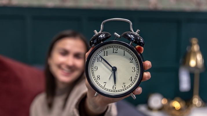 Una mujer sujetando un despertador analógico negro que marca las tres, simbolizando el momento del cambio de hora en España