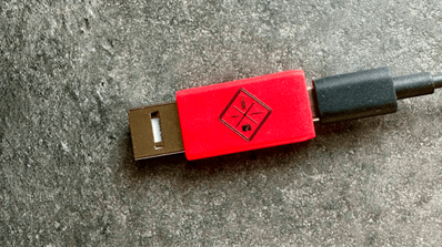 Bloqueador de datos USB de la marca Travel Secure conectado a un cable USB-A blanco sobre fondo neutro.