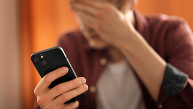 Joven mirando su smartphone con expresión de preocupación, representando la angustia de recibir una llamada de estafa o ciberacoso