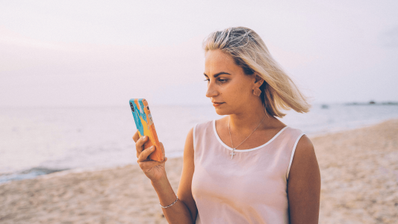 Una chica usando su móvil en la playa