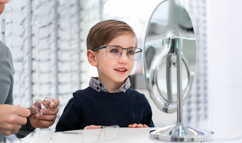 Niño sonriente de unos 8 años probándose unas gafas de montura azul en una óptica, como ejemplo de los beneficiarios del Plan Veo para salud visual infantil