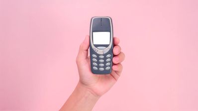 Una persona sostiene un clásico móvil Nokia 3310 en una mano, mientras un smartphone moderno permanece apagado sobre una mesa de madera, simbolizando la elección de la desconexión digital