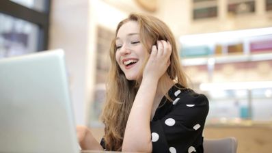 Una chica contenta hablando y mirando el ordenador