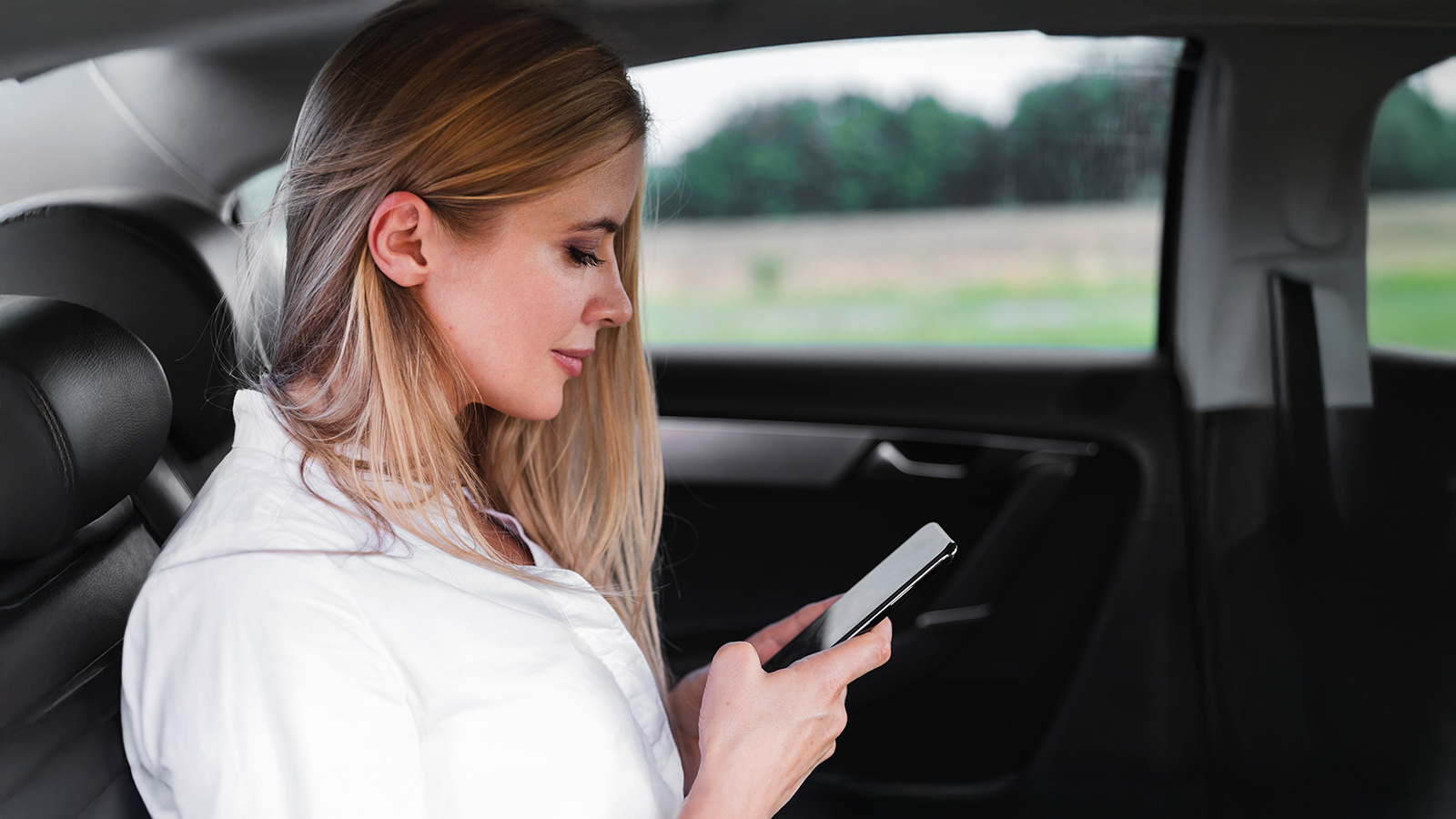Mujer sentada en el asiento trasero de un coche experimentando síntomas de mareo mientras mira la pantalla de su teléfono móvil