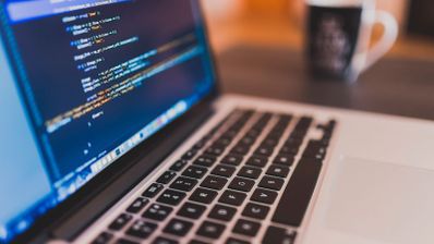 Código de programación en la pantalla de un portátil junto a una taza de café en un espacio de trabajo.