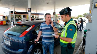 Conductor apagando el motor de su coche junto a un surtidor de gasolinera antes de repostar, siguiendo las normas de seguridad vial establecidas por la DGT en España