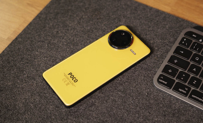 Smartphone POCO de color amarillo con módulo de cámaras circular sobre una superficie gris junto a un teclado