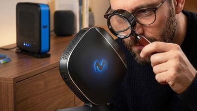 Primer plano de una persona examinando con una lupa el amplificador Smart WiFi de Movistar con el logotipo iluminado en azul.