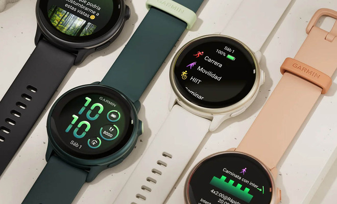 Cuatro relojes inteligentes Garmin alineados mostrando diferentes pantallas de actividad física, esferas digitales y correas en colores negro, verde oscuro, blanco y rosa.
