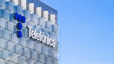 Logotipo de Telefónica sobre la fachada acristalada de su sede corporativa con un cielo azul despejado de fondo.