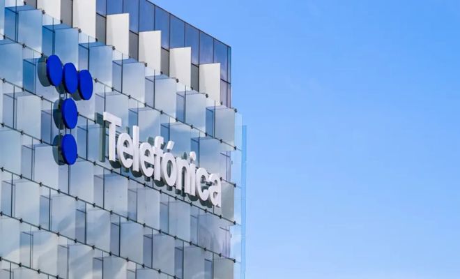 Logotipo de Telefónica sobre la fachada acristalada de su sede corporativa con un cielo azul despejado de fondo.
