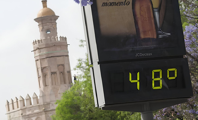 Termómetro urbano en Sevilla marcando 48 grados con la Torre del Oro al fondo bajo un sol intenso.