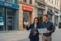 Pareja consultando folletos financieros frente a oficinas de BBVA, Santander y CaixaBank en una calle comercial.