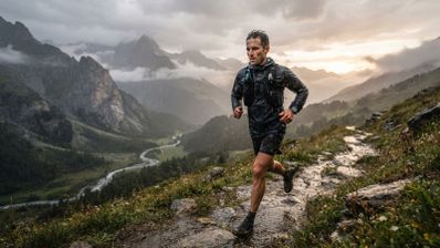 Corredor de montaña con chubasquero y reloj Garmin avanzando por un sendero rocoso bajo la lluvia.