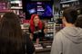 Una dependienta de una tienda GAME muestra la tarjeta del servicio GAME Premium a varios clientes en el mostrador.