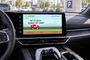 Consola central de un coche mostrando un videojuego de carreras en la pantalla de infoentretenimiento con un mando de consola en la base.