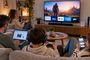 Cuatro personas en un salón consumiendo contenidos en diferentes dispositivos como Smart TV, ordenador portátil, consola de videojuegos y smartphone.