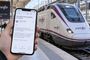 Mano sosteniendo un teléfono móvil con un correo electrónico sobre seguridad de cuenta frente a un tren de Renfe en la estación de Madrid Atocha.